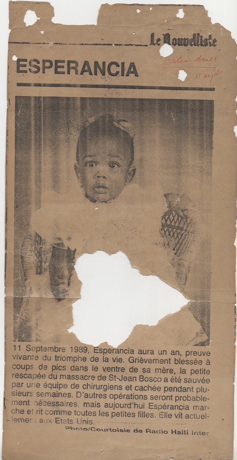 Newspaper clipping photo of a Black baby girl in a white dress with a bow in her hair, sitting on a wicker chair and looking quizzically to the side